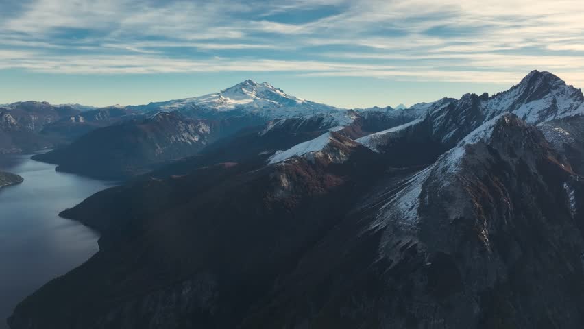 Aerial drone overlooking the snow-covered summit of Cerro Tronador with the deep waters of Brazo Tristeza branch winding through the Andean mountains, Argentina.