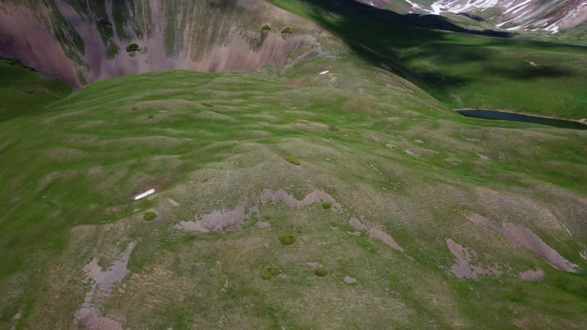 Aerial panning shot starting from dark waters of Lake Silbeli and turning to reveal a second small alpine pond among green ridges in Sairam-Ugam National Park, Kazakhstan.
