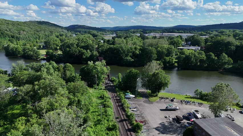 Scenic high-angle aerial drone footage capturing the historic charm of New Milford, Connecticut, located in Litchfield County. The video showcases the beautiful New England suburban landscape, featuring the winding Housatonic River, lush green hillsides, and the classic downtown village green area with its traditional architecture and local streets. Perfect for regional tourism marketing, commercial real estate videos, New England travel documentaries, autumn or summer seasonal concepts, and small-town American lifestyle stock media.