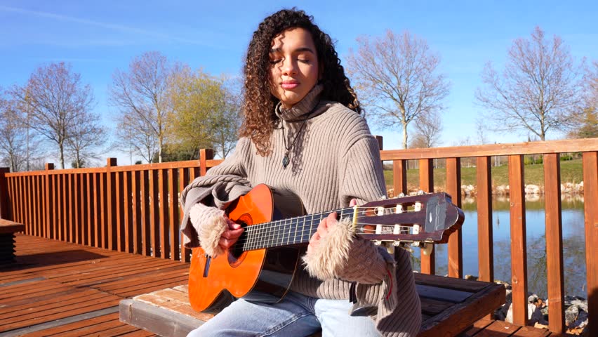 Young woman with curly hair playing the classical guitar in a park on a sunny day