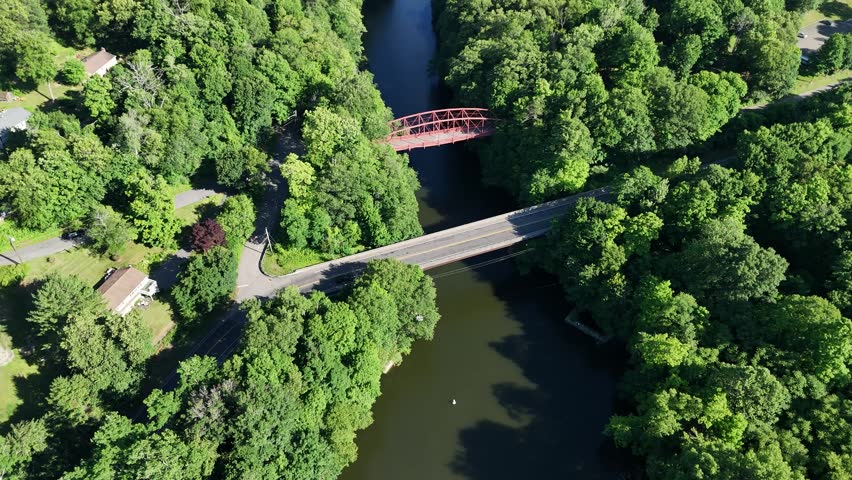 Scenic high-angle aerial drone footage capturing the historic charm of New Milford, Connecticut, located in Litchfield County. The video showcases the beautiful New England suburban landscape, featuring the winding Housatonic River, lush green hillsides, and the classic downtown village green area with its traditional architecture and local streets. Perfect for regional tourism marketing, commercial real estate videos, New England travel documentaries, autumn or summer seasonal concepts, and small-town American lifestyle stock media.