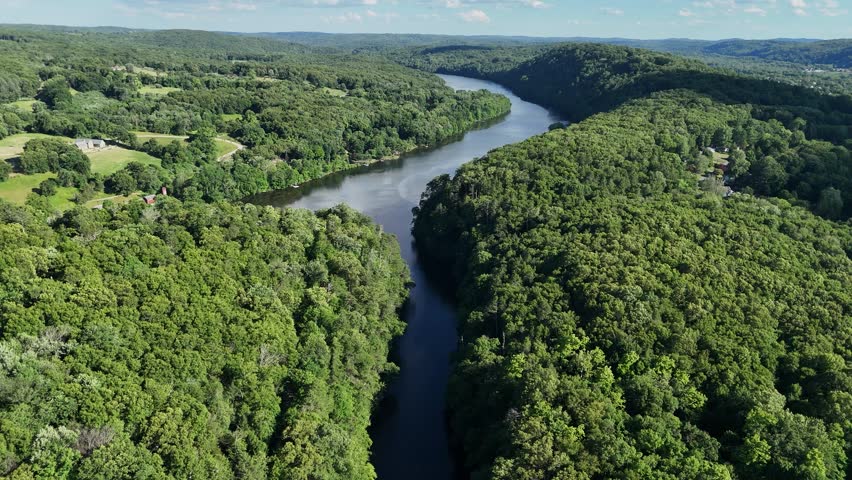 Scenic high-angle aerial drone footage capturing the historic charm of New Milford, Connecticut, located in Litchfield County. The video showcases the beautiful New England suburban landscape, featuring the winding Housatonic River, lush green hillsides, and the classic downtown village green area with its traditional architecture and local streets. Perfect for regional tourism marketing, commercial real estate videos, New England travel documentaries, autumn or summer seasonal concepts, and small-town American lifestyle stock media.