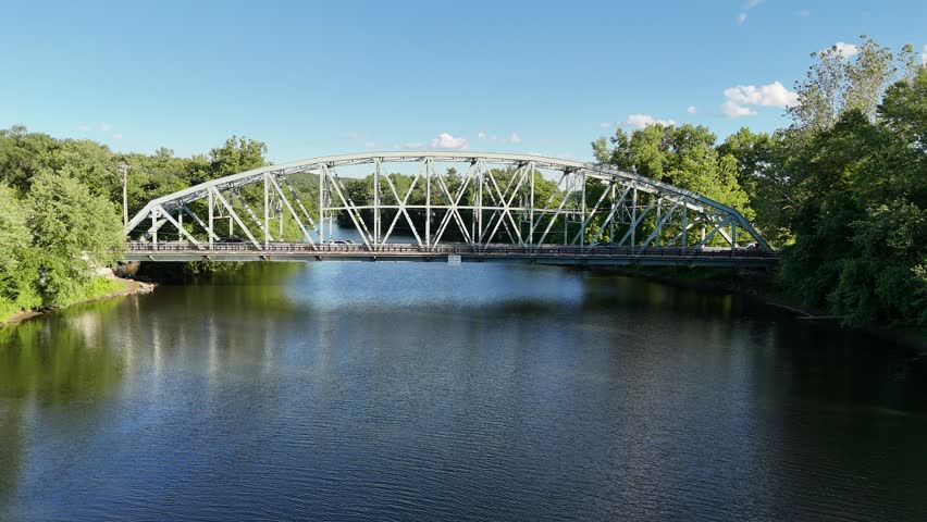 Scenic high-angle aerial drone footage capturing the historic charm of New Milford, Connecticut, located in Litchfield County. The video showcases the beautiful New England suburban landscape, featuring the winding Housatonic River, lush green hillsides, and the classic downtown village green area with its traditional architecture and local streets. Perfect for regional tourism marketing, commercial real estate videos, New England travel documentaries, autumn or summer seasonal concepts, and small-town American lifestyle stock media.