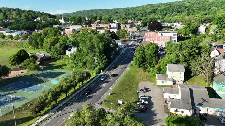 Scenic high-angle aerial drone footage capturing the historic charm of New Milford, Connecticut, located in Litchfield County. The video showcases the beautiful New England suburban landscape, featuring the winding Housatonic River, lush green hillsides, and the classic downtown village green area with its traditional architecture and local streets. Perfect for regional tourism marketing, commercial real estate videos, New England travel documentaries, autumn or summer seasonal concepts, and small-town American lifestyle stock media.