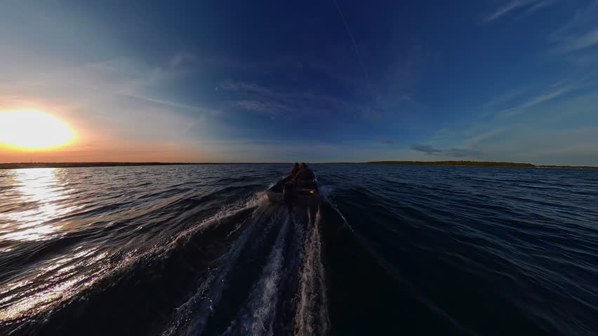Boat speeding at sun set in Lake Couchiching view. Two anglers boating in Canadian lake during fishing prime time. Bass boat with outboard speed motor. Utility boat ride to fishing honey hole spot.