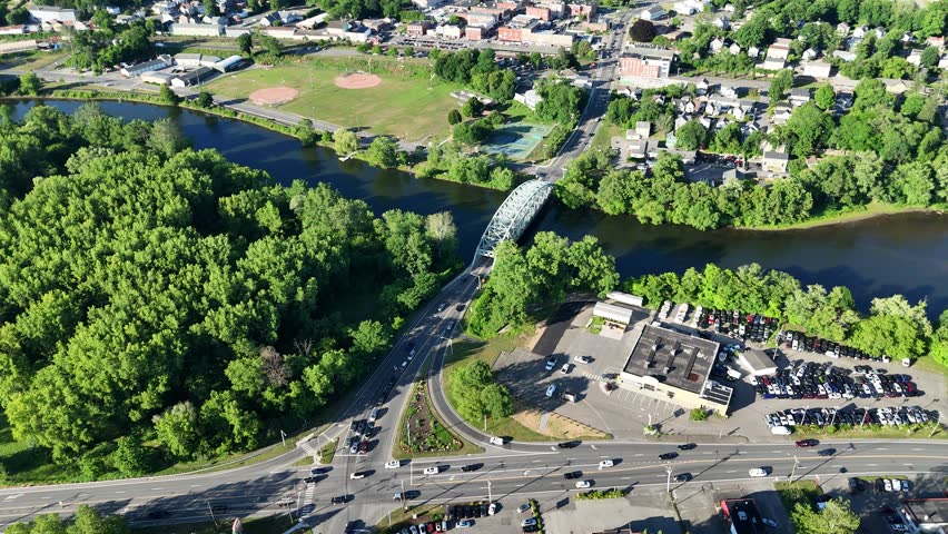 Scenic high-angle aerial drone footage capturing the historic charm of New Milford, Connecticut, located in Litchfield County. The video showcases the beautiful New England suburban landscape, featuring the winding Housatonic River, lush green hillsides, and the classic downtown village green area with its traditional architecture and local streets. Perfect for regional tourism marketing, commercial real estate videos, New England travel documentaries, autumn or summer seasonal concepts, and small-town American lifestyle stock media.