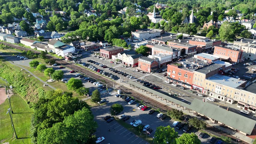 Scenic high-angle aerial drone footage capturing the historic charm of New Milford, Connecticut, located in Litchfield County. The video showcases the beautiful New England suburban landscape, featuring the winding Housatonic River, lush green hillsides, and the classic downtown village green area with its traditional architecture and local streets. Perfect for regional tourism marketing, commercial real estate videos, New England travel documentaries, autumn or summer seasonal concepts, and small-town American lifestyle stock media.