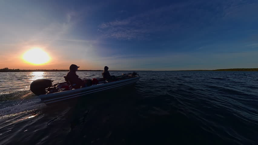 Boat speeding at sun set in Lake Couchiching view. Two anglers boating in Canadian lake during fishing prime time. Bass boat with outboard speed motor. Utility boat ride to fishing honey hole spot.