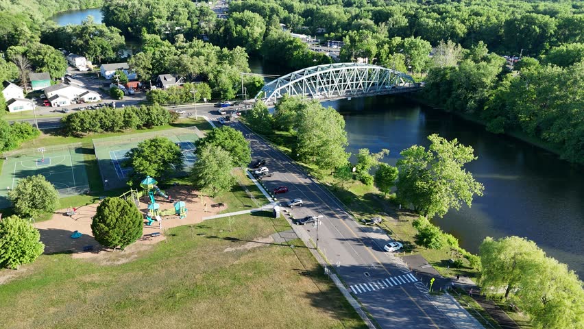 Scenic high-angle aerial drone footage capturing the historic charm of New Milford, Connecticut, located in Litchfield County. The video showcases the beautiful New England suburban landscape, featuring the winding Housatonic River, lush green hillsides, and the classic downtown village green area with its traditional architecture and local streets. Perfect for regional tourism marketing, commercial real estate videos, New England travel documentaries, autumn or summer seasonal concepts, and small-town American lifestyle stock media.