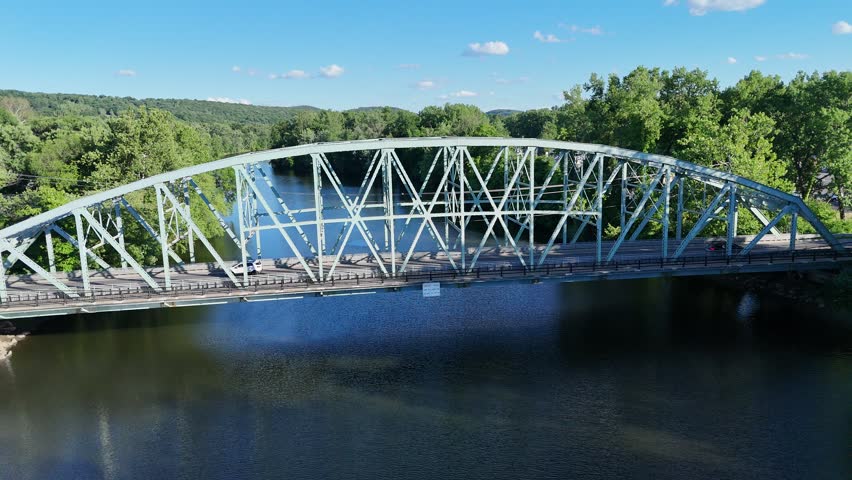 Scenic high-angle aerial drone footage capturing the historic charm of New Milford, Connecticut, located in Litchfield County. The video showcases the beautiful New England suburban landscape, featuring the winding Housatonic River, lush green hillsides, and the classic downtown village green area with its traditional architecture and local streets. Perfect for regional tourism marketing, commercial real estate videos, New England travel documentaries, autumn or summer seasonal concepts, and small-town American lifestyle stock media.
