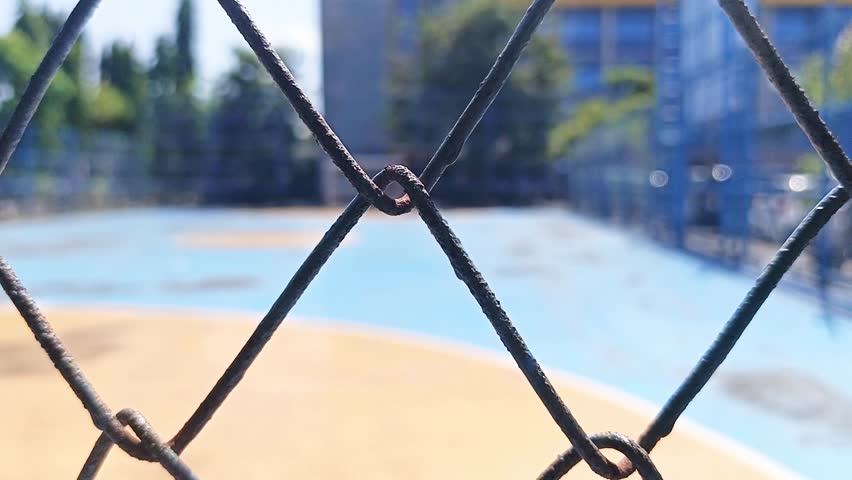 Close up of a metal chain link fence with a blurred outdoor sports court background