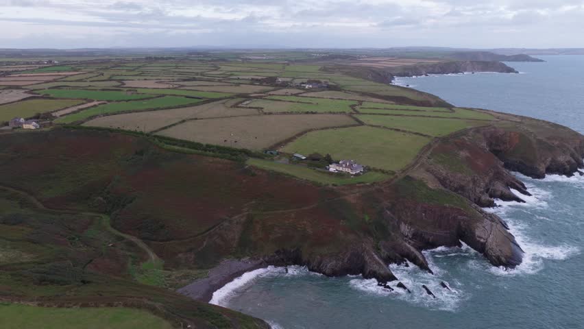 Aerial view of the rugged Welsh Coast with steep cliffs, green pastures, and waves crashing against the shore in St Davids, Wales, United Kingdom.