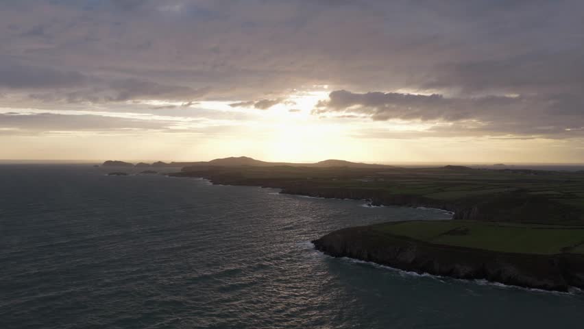 Aerial view of the sunset over the rugged Welsh Coast with green fields and cliffs in St Davids, Wales, United Kingdom.
