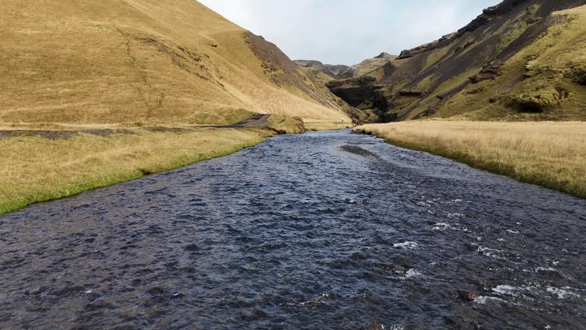 Aerial view of a river flowing through a valley with grassy hills and rocky slopes near Kvernufoss in Evindarholar, Rangarthing eystra, Iceland.