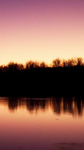 Vertical video capturing a colorful sunset over a large lake in a Canadian national park. Golden and orange hues reflect across the calm water, creating a serene wilderness landscape.