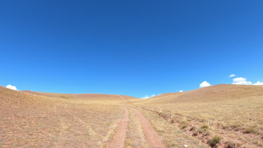 Video of a car driving along a country road under blue sky. Altai desert and semi-desert environment.