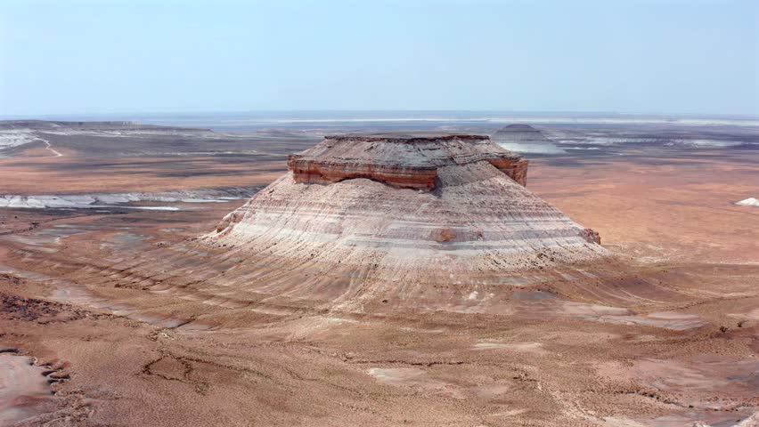 Aerial drone flies forward above Bozzhyra landscape in Mangistau Kazakhstan revealing isolated chalk mesa with layered limestone cliffs, vast desert plateau and dramatic geological formations
