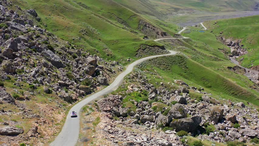 Aerial drone shot of winding mountain road leading through green hills and rocky terrain in Azerbaijan, showcasing natural landscape patterns, scenic travel route, curved pathway, highland environment