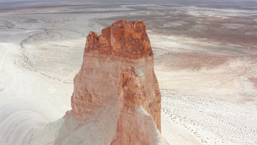 Aerial close drone view of towering Bozzhyra rock pinnacle in Mangistau Kazakhstan, highlighting dramatic erosion, white desert terrain and ancient ocean landscape