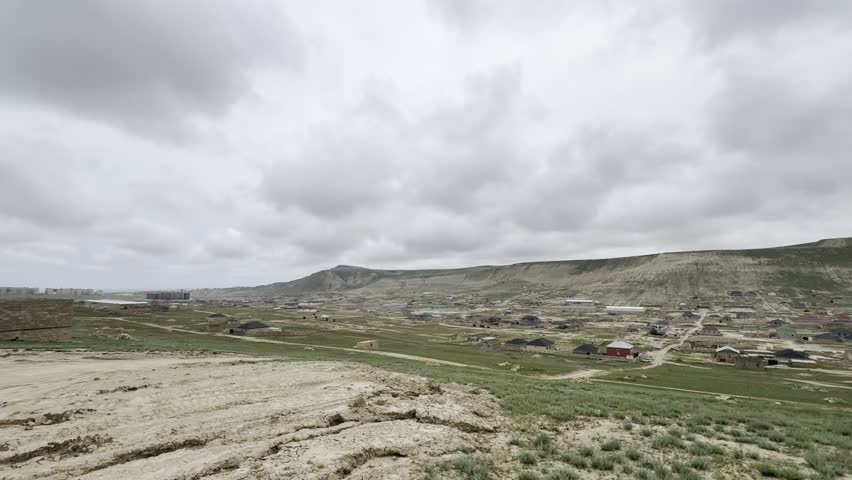 Panoramic view of hills in cloudy weather, with newly built houses seen in the distance at the foot of the hills.
