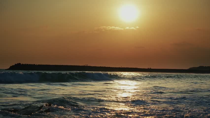 Aerial view of ocean waves rolling onto the shore at golden hour with a rocky island off the coast of India