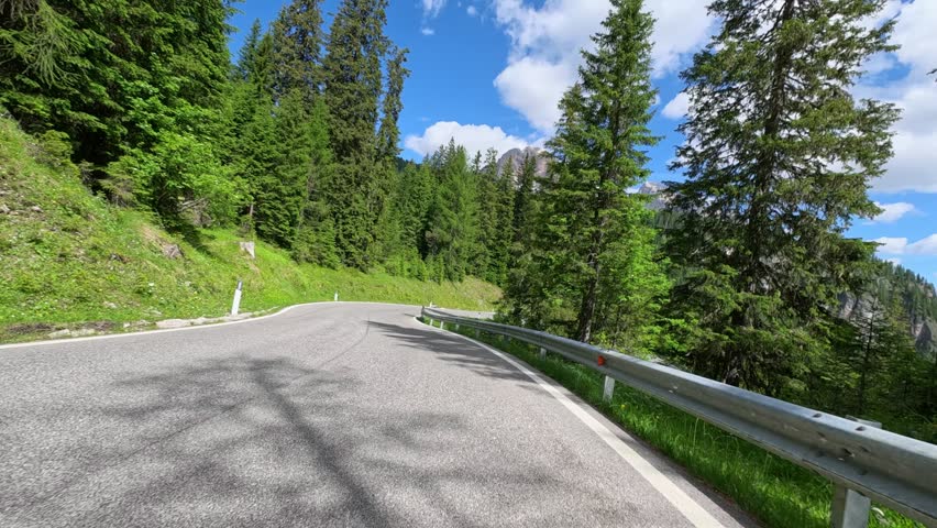 Motorcycle tilting and banking hard on serpentine mountain pass road, dynamic speed trip through coniferous woods in summer. Fast motorcycling adventure in Dolomites. POV motorbike ride