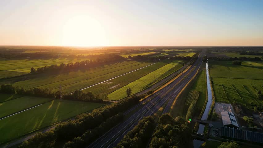 Stunning golden sunrise casts warm light over expansive green fields and a winding highway, highlighting tranquility in a rural setting with distant horizons.