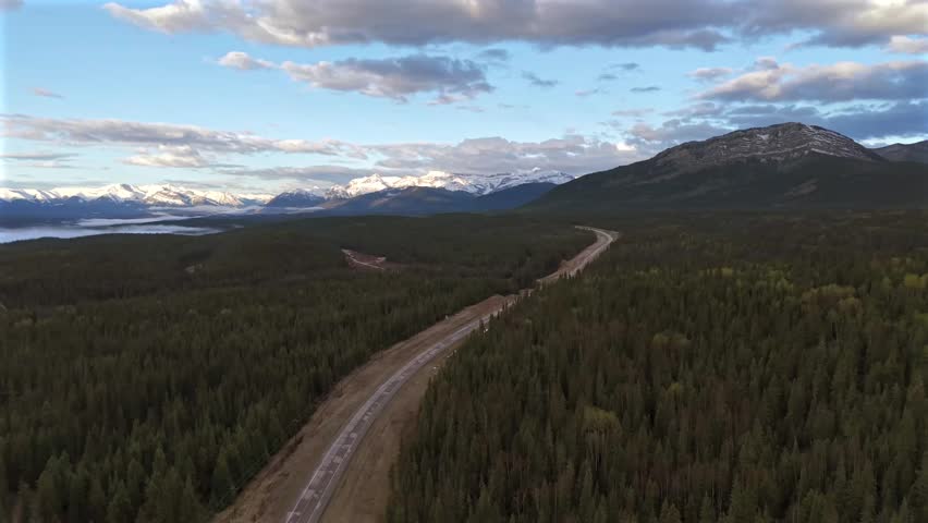 Forward moving and panning aerial drone footage of an empty road through pine forest in the Canadian Rockies with morning fog conditions.