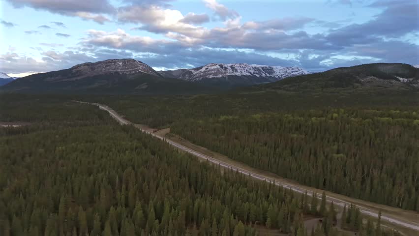 Panning and rotating aerial drone footage of an empty road in the Canadian Rockies near Banff National Park with morning fog and soft light.