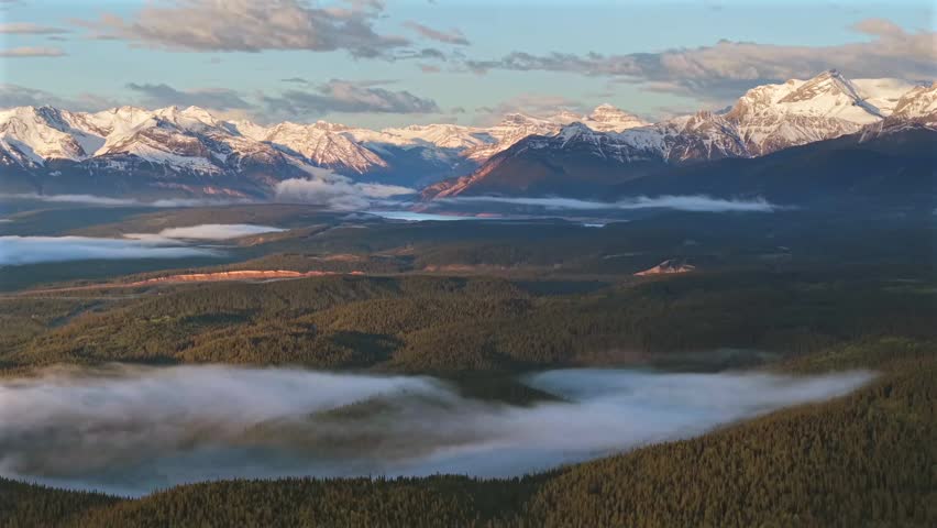 Forward panning aerial drone footage of the Canadian Rockies near Banff National Park with morning fog and a temperature inversion across the mountain landscape.