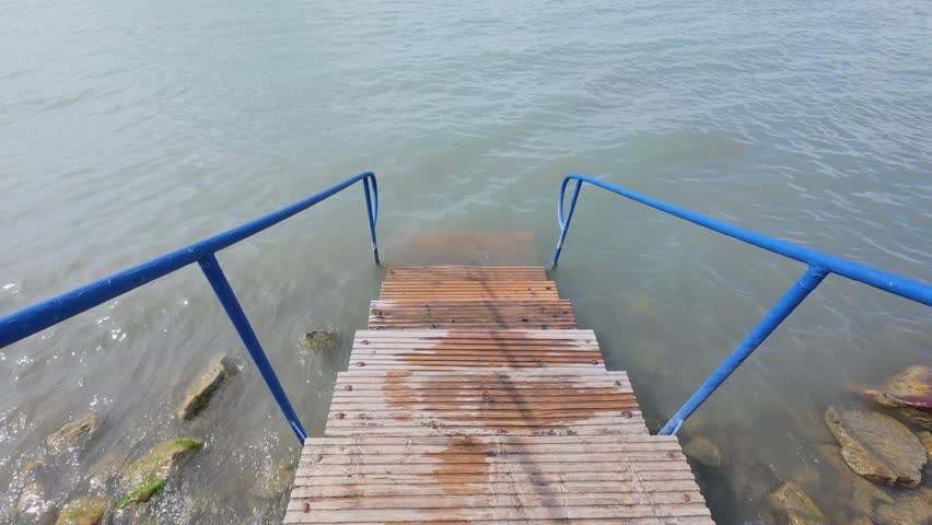 Siofok Hungary May 31 2026. Wooden access platform with blue railings leading into the waters of Lake Balaton on a sunny day with gentle waves.