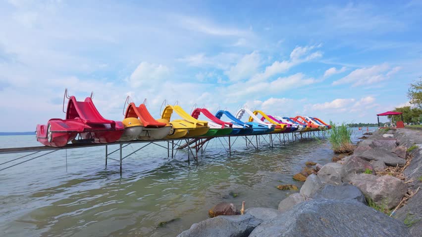 Siofok Hungary May 31 2026. Colorful pedal boats stored on a lakeside platform above the water at a recreational waterfront area under a cloudy sky.