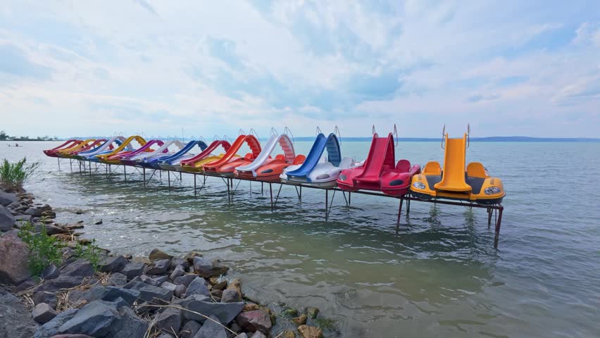 Siofok Hungary May 31 2026. Colorful pedal boats stored on a dock above the water at a recreational lakeside area under cloudy skies.