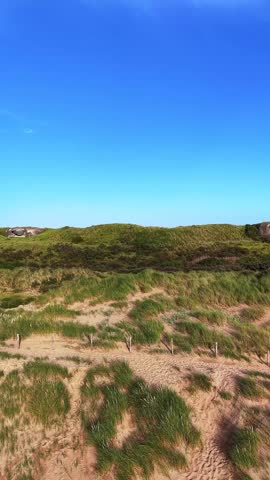 A sandy path winding among grass-covered dunes toward a wooden fence.
