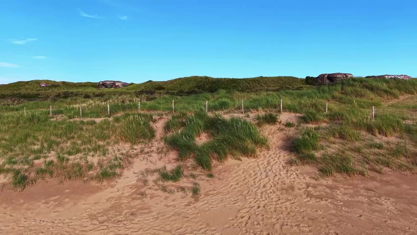 A sandy path winding among grass-covered dunes toward a wooden fence.