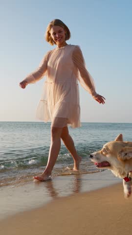 Woman walking beach with corgi dog seaside summer joyful lifestyle vertical reel coastal background