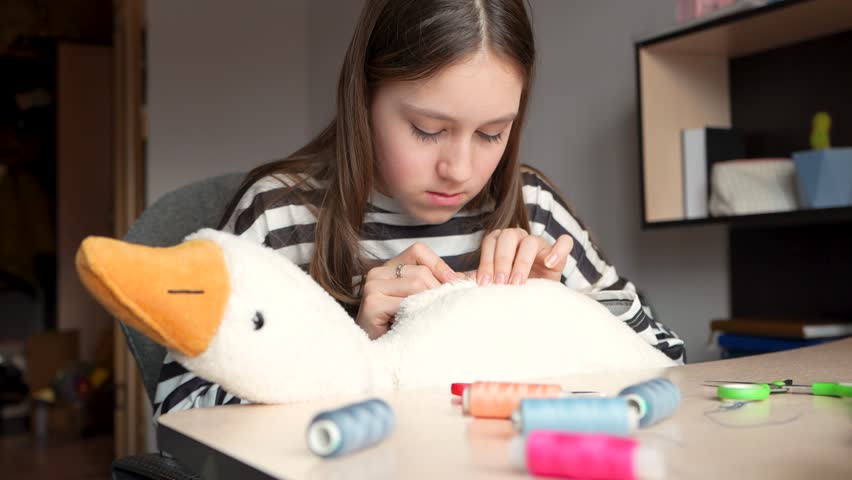 A little girl sews a felt toy while sitting at table