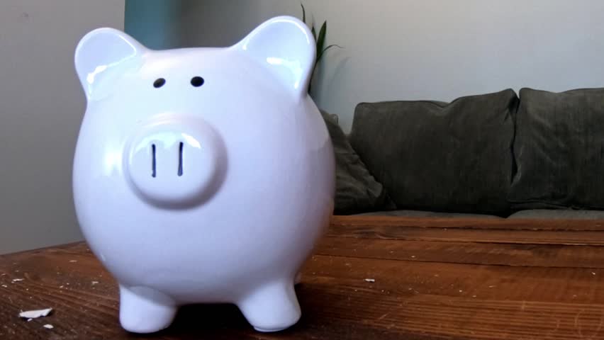 Extreme close up showing a hand smashing a white porcelain piggy bank with a sledgehammer. The ceramic bank did not break completely.