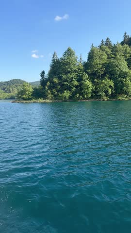 View of Plitvice Lakes with forest island and clear water under blue sky. The video represents concepts of nature, travel, national park and peaceful landscape scenery.