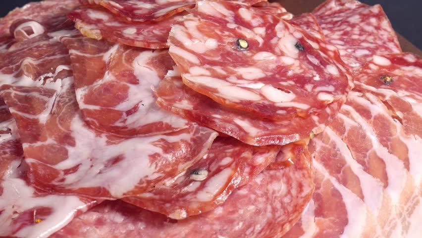 meat platter rotating with assortment of various spanish, french or italian appetizers - sliced prosciutto, parma sausage, ham, boiled pork, salami, close up