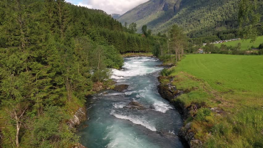 Dynamic glacial water rapids flow through forest mountains.