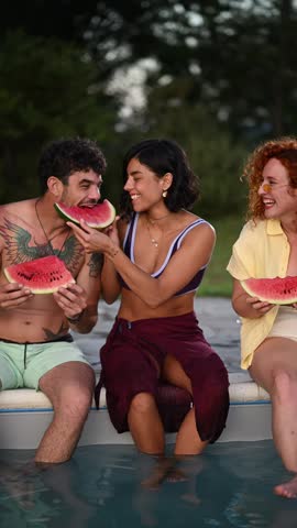 Group of diverse friends having fun and eating fresh watermelon slices. Young smiling couple enjoying a summer day at the swimming pool