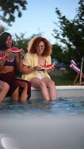 Young friends sitting on the edge of a swimming pool, eating fresh watermelon slices and enjoying a relaxing summer afternoon together