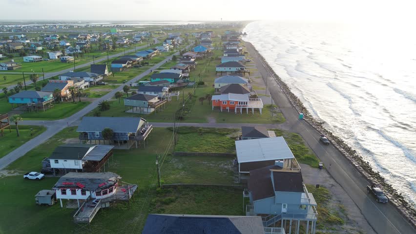 Seawall coastal frontage Surfside Beach corridor along Seashell Dr borders stone lined barrier with elevated homes facing Gulf horizon. Sunlit roofing, surf highlights extend in Freeport, Texas. USA