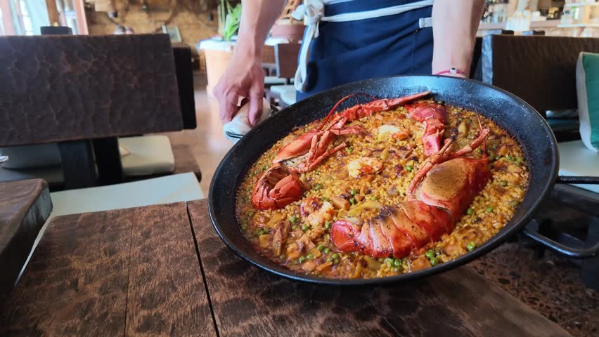 Mallorca Spain Europe. 01.06.2026. Video. A close-up view of a vibrant seafood paella dish featuring succulent lobster tails and green peas, presented in a rustic pan on a wooden table
