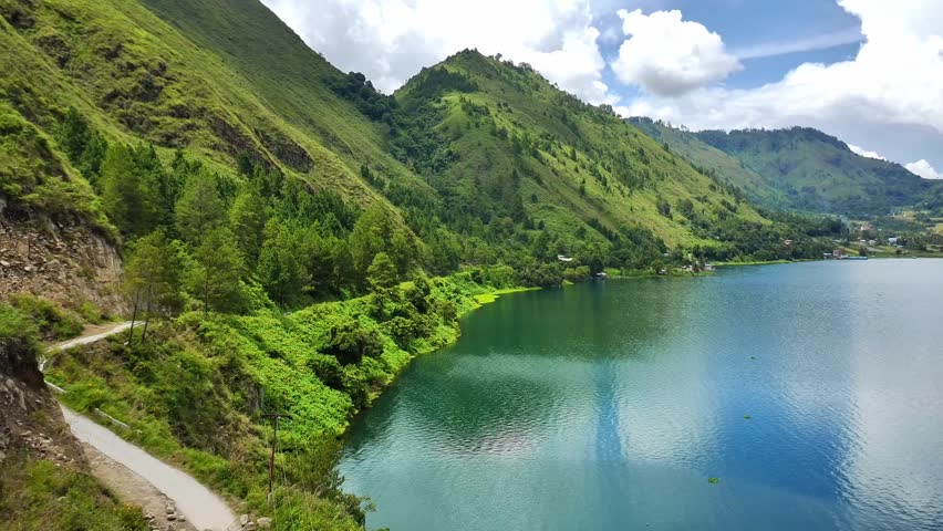 Aerial drone footage capturing a vertical ascent over the scenic Lake Toba landscape, revealing lush green hills, forested slopes, and calm blue water. High-resolution 4K nature video showcasing Indonesia’s volcanic mountain scenery, tropical environment, and breathtaking travel destination from above
