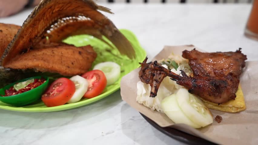 Indonesian fried fish and grilled chicken served with sambal, tomato, cucumber, cabbage, and tofu, close-up street food footage with vibrant presentation.