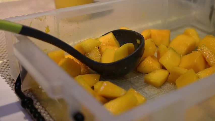 Gloved hands preparing a layered mango dessert drink with fresh mango cubes and cream in a plastic cup, close-up tropical beverage footage.
