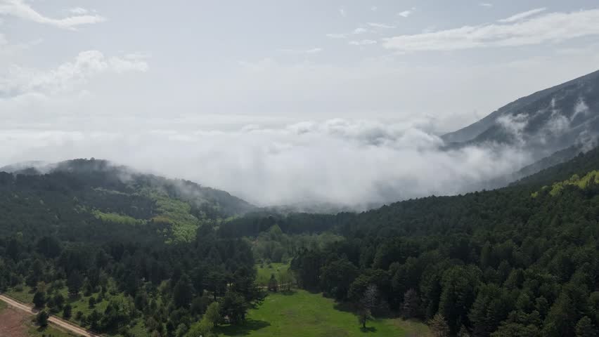 An aerial shot of a vast green mountain forest landscape with low clouds rolling through the valley.