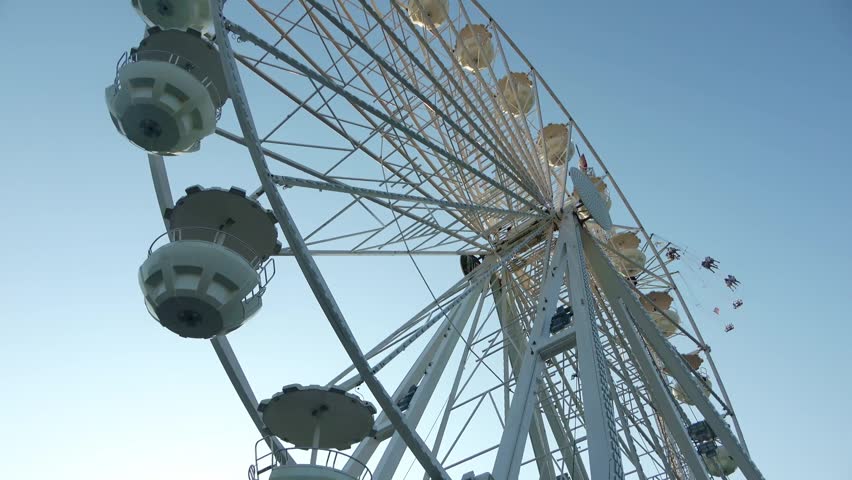 Giant white Ferris wheel spinning against a clear blue sky at a fairground on a sunny summer day